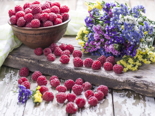 Fresh ripe juicy raspberries in a bowl with flowers on a wooden old background, decorated with a textile towel.