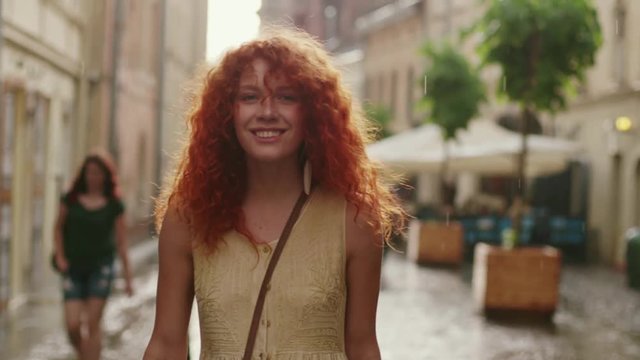 Close up attractive woman with red curly hair walking in the rain on the street look at camera spinning happy smile cute fashion water silhouette summer face female lonely stop