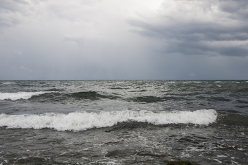 Coast of the Black Sea. Surf. Light breeze. Small waves, with white foam, from the water. The color of sulfur, black, blue.
