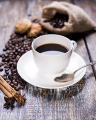 Coffee in a cup, coffee beans, spice, cookies in the shape of heart on a wooden background.