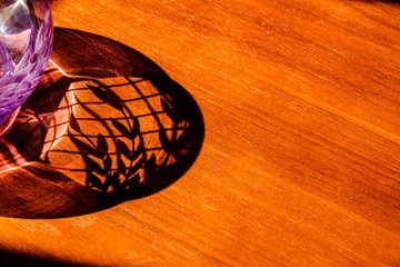 Sunlight shining through a crystal vase to produce a nice shadow effect on a wooden table.