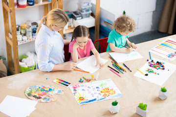 High angle portrait of two children enjoying art and craft lesson with young teacher in development school, copy space
