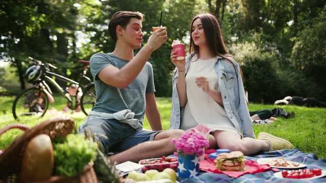 Happy young beautiful couple smiling resting in park have picnic talk drink man eat apple woman tree love girl summer nature emotive outdoors outing pleasure positive pretty relations