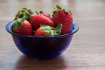 Heap fresh strawberries in the blue glass bowl on the rustic wood table