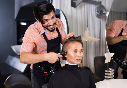 Cheerful male professional shaving female's hair