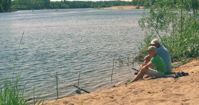 Happy father and son are sitting on the river bank, fishing, dad and son are fishing in the morning. Happy family.