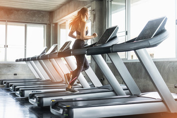 Cute young woman exercising on  treadmill at a gym.Active young woman running on treadmill. smile...