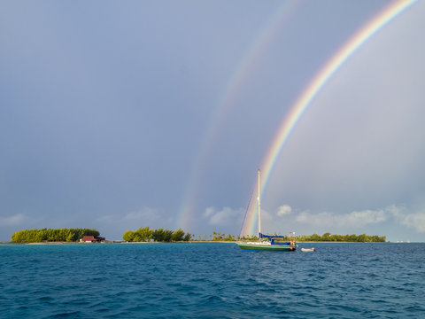 sailing yacht anchoring under a rainbow in the shallow, turquoise lagoon of the Makemo Atoll, Tuamotus, French Polynesia