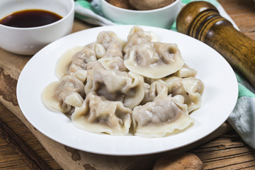 Close up fresh boiled dumplings with hot steams on wood plate. Chinese food on rustic old vintage wooden background.