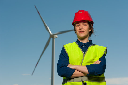 Portrait of a handsome successful young woman the chief designer in a green waistcoat and a red helmet against the background of windmills and a blue sky.