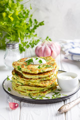 Zucchini pancakes with parsley and sour cream, summer food, tasty snack. High stack in a plate on white wood