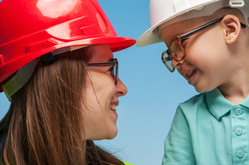 Close-up of a positive young mother engineer and son in a helmet and glasses looking at each other. Concept of future development of energy and succession of generations