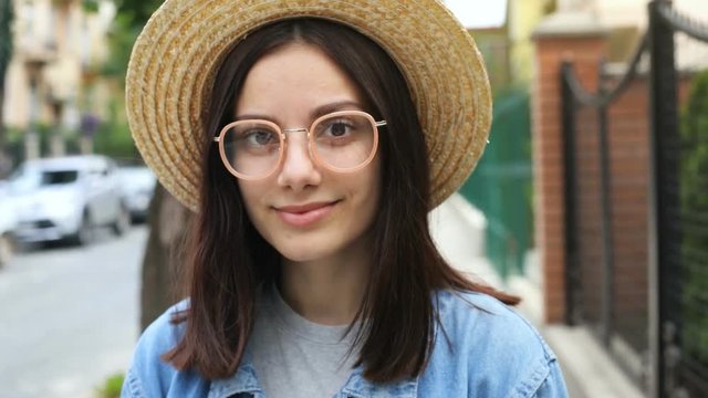 outdoor portrait of young beautiful happy smiling girl with eyeglasses brunette hair wearing straw hat smiling and looking at camera calm peaceful smile attractive woman summer female fashion look