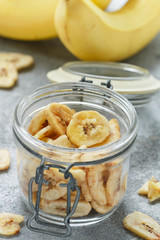 Homemade dried banana chips in a glass jar and fresh bananas.  Yellow fried fruit slices. Healthy sweet snack. Vegetarianism
