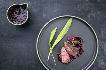 Modern Barbecue dry aged Hirsch Filet Steak aufgeschnitten mit Bärlauch und Preiselbeeren Sauce als Draufsicht auf einem Teller 