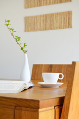 white cup, book and vase on natural oak table