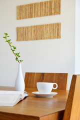 white cup, book and vase on natural oak table
