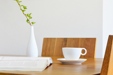 white cup, book and vase on natural oak table