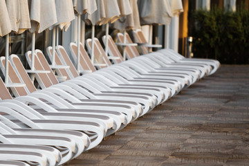 Fototapeta na wymiar Row of white plastic deck chairs with umbrellas near the swimming pool. holidays concept