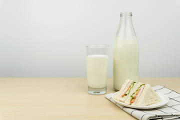 a glass of milk with milk bottle and the club sandwiches in a white round dish on the wooden table.
