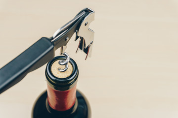 close up of a metal corkscrew or waiter's friend with a bottle of red wine