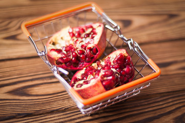 Full metal market basket with orange rubber handles of halves of red ripe fresh pomegranate on old brown weathered rustic planks