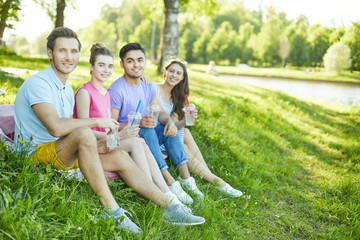Fototapeta premium Row of young friends sitting on green lawn in park on sunny day and enjoying rest