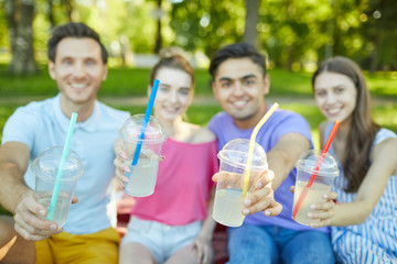 Four drinks in plastic glasses held by friendly teens during their outdoor gathering in park