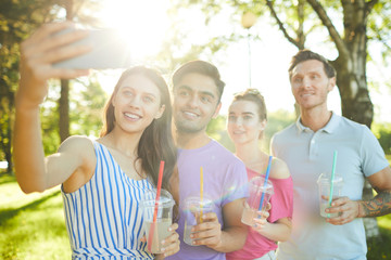 Row of four happy teens posing for selfie during outdoor relax on summer day