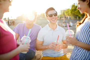 Laughing guy with drink having talk with friends during picnic on summer day