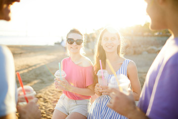Fototapeta na wymiar Two smiling girls with drinks talking to their boyfriends on sunny day on the beach