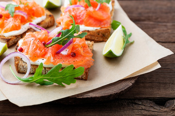 Smoked salmon sandwich with cream cheese on wooden table.