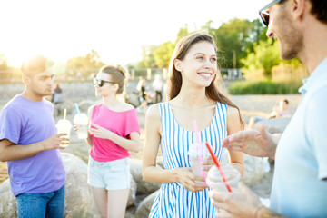 Happy girl with drink talking to her boyfriend on background of another couple on the beach