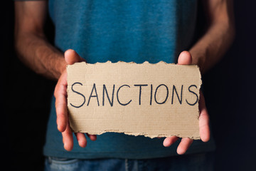 Man showing worn rectangle cardboard with handwritten inscription sanctions on black background