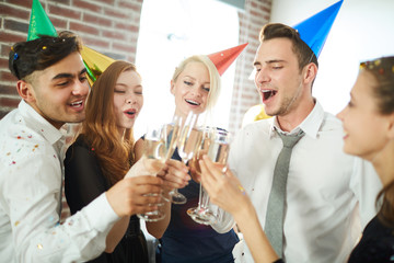 Several excited young people making birthday toast for one of them at home party