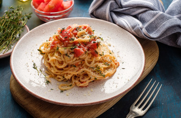 Spaghetti with tomatoes and thyme in a plate on a blue table