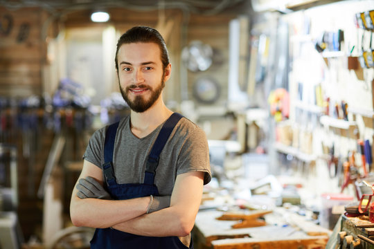 Young cross-armed woodworking master looking at camera inside his workshop