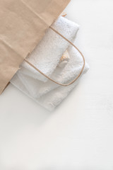Folded two white towels in a paper bag on a white wooden table. Spa and wellness, cotton terry textile. Ecological theme