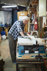 Aged man in workwear and gloves standing by processing machine in his workshop