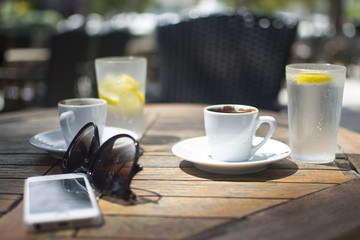 cups of coffee and mineral water with lemon in a glass are on the table, next glasses and phone are lying on the table