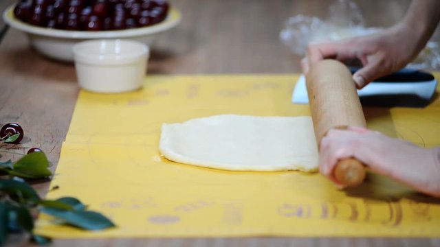 Woman hands roll out the dough on the kitchen table to make a pie with berries.