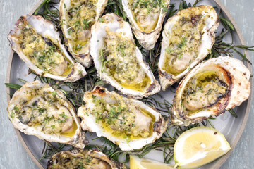 Barbecue overbaked fresh opened oyster with garlic, lemon and herbs offered as top view on a plate