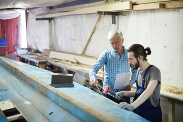 Senior engineer with paper pointing at one of boards of vessel construction while instructing his...