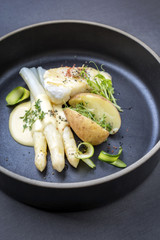 Modern German fried cod fish filet with white asparagus in hollandaise sauce und roast potatoes as top view on a plate