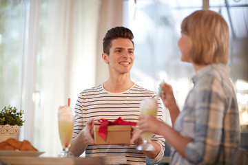 Young man with giftbox looking at his girlfriend and congratulating her on life event or occasion