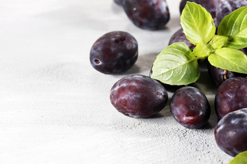 Plums on white stone background. Half of blue plum fruit. Many beautiful plums with leaves.