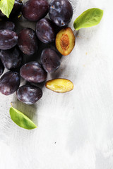 Plums on white stone background. Half of blue plum fruit. Many beautiful plums with leaves.