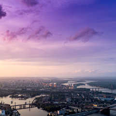 Panoramic view of a modern city with a river, unfinished bridge and park part of the city. Skyline bird eye aerial view with industrial zone and high-rise residential area under dramatic cloud sunset