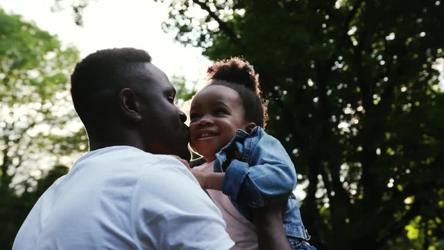 Close up african father hugging his daughter play holds on hands twists spending holiday together in park family affection smile happy slow motion love child summer man kid sun girl parenting outdoors