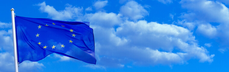 Flag of the European Union waving in the wind on flagpole against the sky with clouds on sunny day, banner, close-up